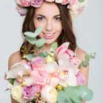 Lovely cheerful female in rose wreath showing bouquet of flowers