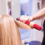 Unrecognizable hairdresser creating hairstyle for her beautiful blond client.