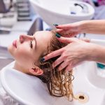 Unrecognizable professional hairdresser washing hair to her client