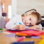 Cute little girl with braids drawing on colorful papers