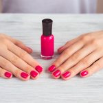 Female hands with pink manicure and a bottle of lacquer on a woo